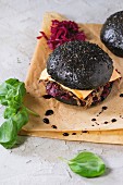 Black burger with beef stews, cheese, red cabbage and balsamic sauce served on baking paper with fresh basil