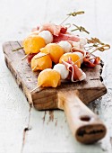 Spiesschen mit Melonenkugeln, Mozzarella und Schinken auf Holzbrett
