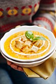 Woman holding pumpkin soup with croutons, cream and basil