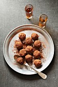 Chocolate truffles on an aluminum plate with two glasses of liqueur on background