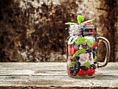 Detox-Drink mit frischen Beeren, Minze und Eis im Glas auf Holzuntergrund