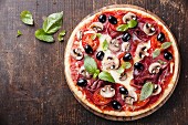 Italienische Pizza mit Salami, Pilzen und Oliven auf Holztisch
