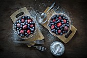Berry tartetelets with icing sugar in baking dishes on wooden plates with sifter and cake forks
