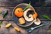 Whole and slice tangerines with leaves on ceramic plate over old wooden table