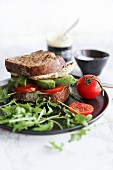 A chicken sandwich with tomato, avocado and rocket