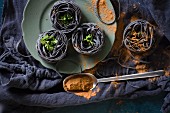 Black ribbon noodles with parsley and spilled spices on a black cloth
