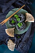 Black ribbon noodles with parsley and small newspaper fans on a turquoise plate