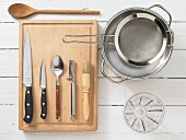 Various kitchen utensils: pot, sieve, measuring cup, knives, spoon, pastry brush, peeler