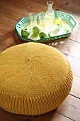 Yellow knitted pouffe next to apples and glasses on green tray