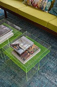 Art books on transparent coffee tables in front of green sofa