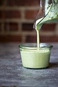 A person is pouring green cashew sauce into a clear jar