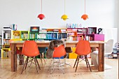 Orange shell chairs and long wooden table in front of colourful shelves