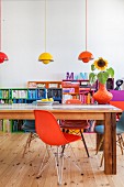 Various designer chairs and wooden table in front of colourful shelves