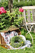 Picnic basket, blanket, enamel crockery and wreath of wildflowers in garden