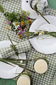 Dekorierte Kerzen und buntem Wiesenblumenstrauß auf grün-weiss karierter Tischdecke