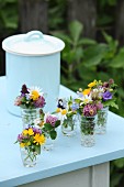 Small glass vases of colourful wildflowers on pale blue table