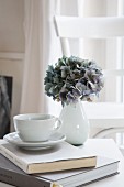 Hortensienblüte in weisser Vase und Tasse auf Buch