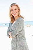A blonde woman wearing a grey cardigan on the beach