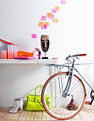Neongelbe Handtasche auf Holzboden neben weissen Stiefeletten und angelehntem Fahrrad; pinkfarbene Post-Its als Wanddekoration