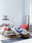 Salmon-pink armchair, full-length mirror and baskets next to bed in bedroom in shades of blue