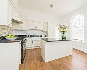 A natural white country house kitchen with a breakfast bar in an old building with round arch windows