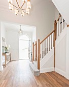 A staircase with a grey carpet in an elegant entrance with an open front door