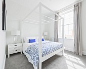 A bedroom with a white four poster bed and a grey carpet