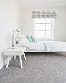 A white bed and a bedside table on a grey carpet