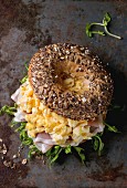 Opened Whole Grain bagels with scrambled eggs, pea sprout and prosciutto ham