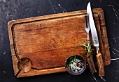 Messer, Gabel, Gewürze und Rosmarin auf Holzschneidebrett (Aufsicht)