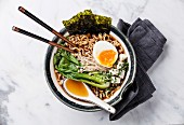 Miso Ramen Asian noodles with egg, enoki and pak choi cabbage in bowl on white marble background