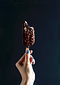 A hand holding a chocolate ice cream lollipop