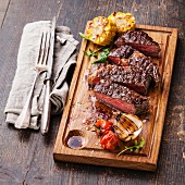 Sliced medium rare grilled Beef steak Ribeye with corn and cherry tomatoes on cutting board