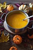 Pumpkin and sweet potatoes soup in a cooking pot, Autumn leaves and different pumkins varieties on a rustic wooden table