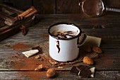 Emaillebecher mit heißer Schokolade und Mandeln auf altem Holztisch