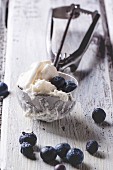 Ice cream in metal spoon with blueberries on white wooden table
