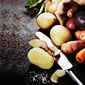 Wurzelgemüse (Kartoffeln, Zwiebeln, Karotten), eine Kartoffel geschält.