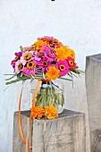 Colourful bouquet of zinnias and tagetes in glass vase on wooden block