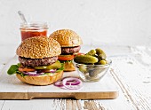 Two fresh homemade burgers served with pickles and onion rings on wooden serving board over white background