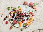 Gesunde Sommerfrüchte: Süße Kirschen im Glas, Pfirsiche, Erdbeeren und Minze auf weißer Servierplatte