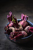 A bunch of red beets with their leaves cut off in a dark wood bowl
