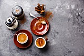 Kaffee in Tassen mit Zimt und Zuckerstreuer auf grauem Untergrund
