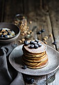 Breakfast table with pancakes served with blueberries and icing sugar and yogurt with muesli