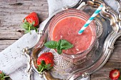 Ein Glas Erdbeer-Smoothie mit Chiasamen, serviert mit Trinkhalm, frischer Minze und Erdbeeren