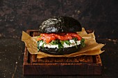 Black Salmon burger with cream cheese and arugula on dark wooden background