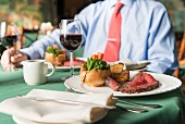 Roastbeef mit Yorkshire Pudding, Gemüse und Wein auf Restauranttisch