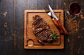 Grilled Steak Striploin and red wine on cutting board on dark wooden background
