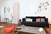 Black couch, coal scuttle, pink retro cabinet and orange pouffe in open-plan living area