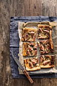 Sliced fig blue cheese and rosemary tart on baking tray with knife on grey background