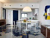 View past dining table into open-plan kitchen with hexagonal floor tiles